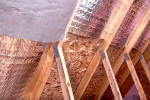 Insulation of attic with fiberglass cold barrier and reflective heat barrier